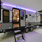 Door Side View from Rear- Awning Extended with LED Lights (Shown in Purple), Two Exterior Doors Opened Up with Optional Solid Steps and Flip-down Steps May Show Optional Features. Features and Options Subject to Change Without Notice.